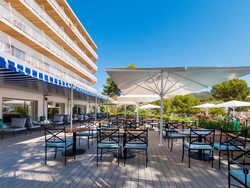 Terrasse d'hôtel avec tables, chaises et grands parasols sous un ciel clair.