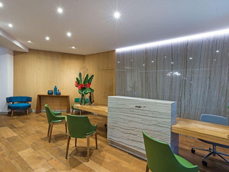 Hall d'accueil moderne avec sol en bois, chaises vertes et réception minimaliste.