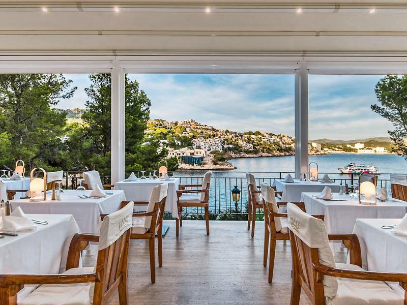 Restaurant élégant avec des tables blanches et vue sur une ville côtière au bord de la mer.