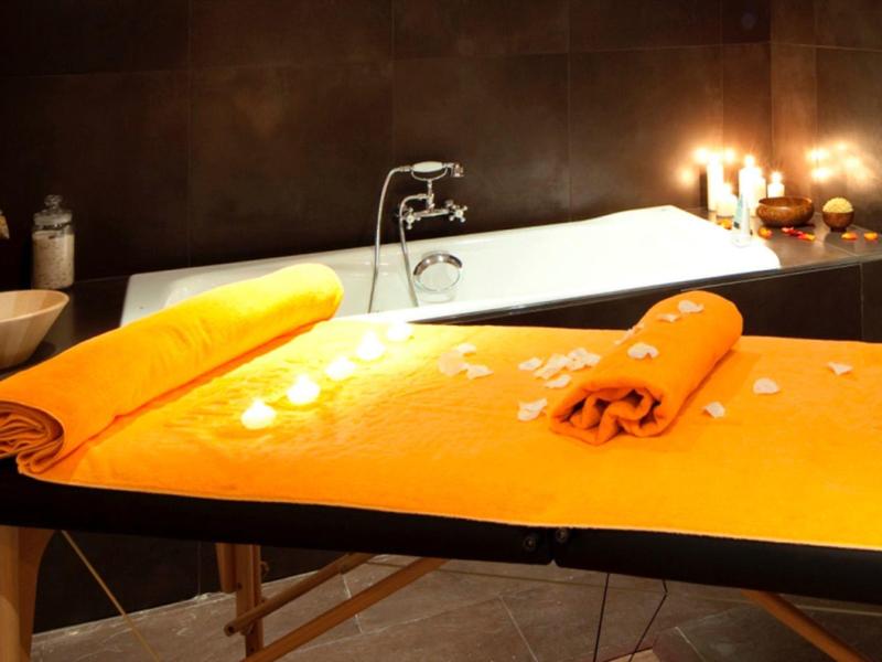 Un espace spa éclairé avec une table de massage et une baignoire en arrière-plan.