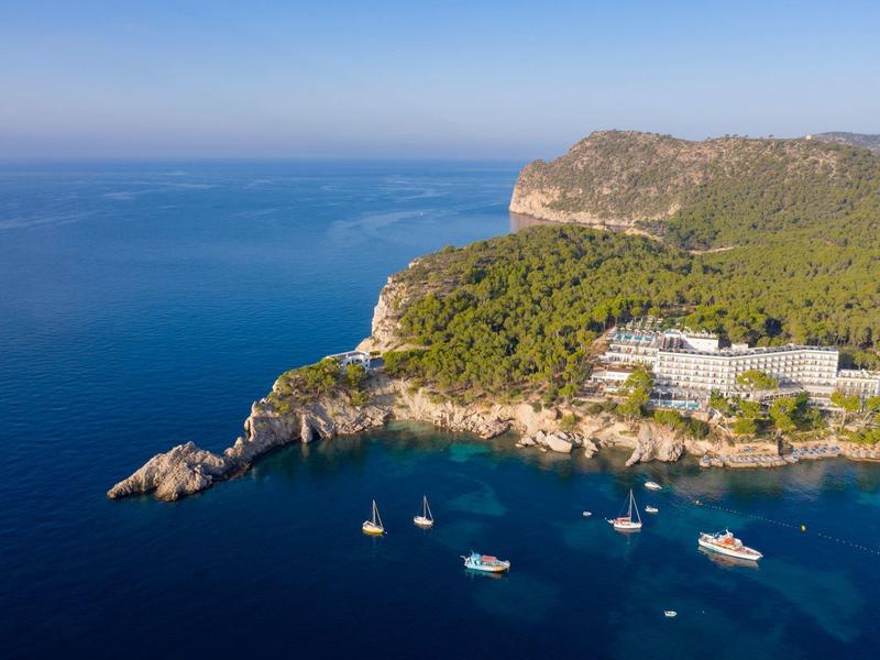 Hôtel côtier entouré de forêt et de mer bleue claire avec des bateaux sur l'eau.