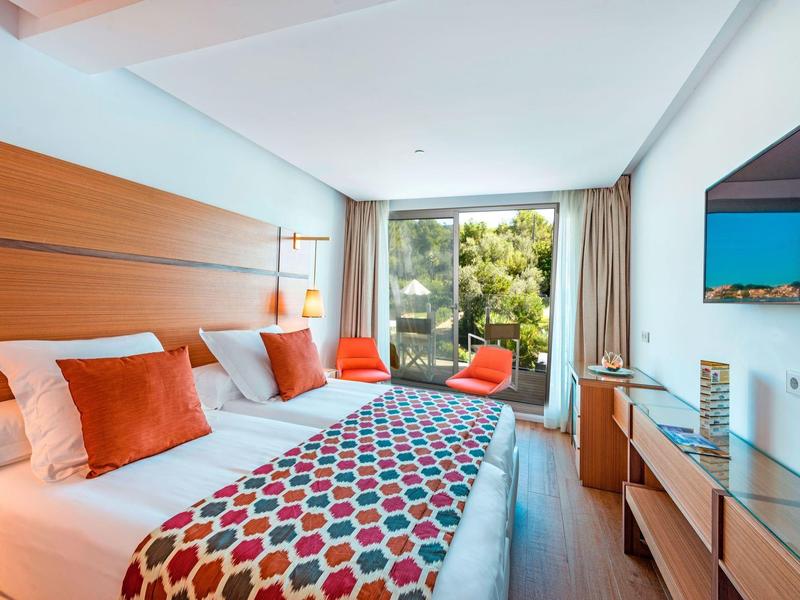 Chambre d'hôtel moderne avec grand lit double, coussins colorés et vue sur le jardin