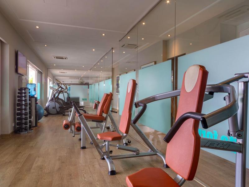 Salle de sport moderne avec équipements de musculation rouges et sol en bois.