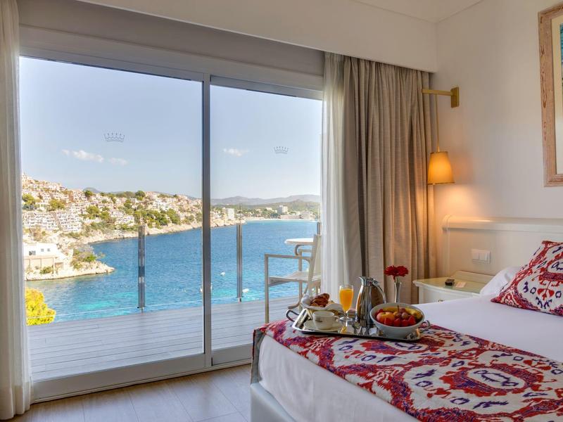 Chambre d'hôtel lumineuse avec balcon et vue sur la mer bleue et la côte.