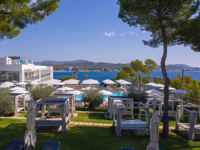 Espace extérieur moderne d'un hôtel avec sièges blancs, vue sur la mer et des arbres en arrière-plan.