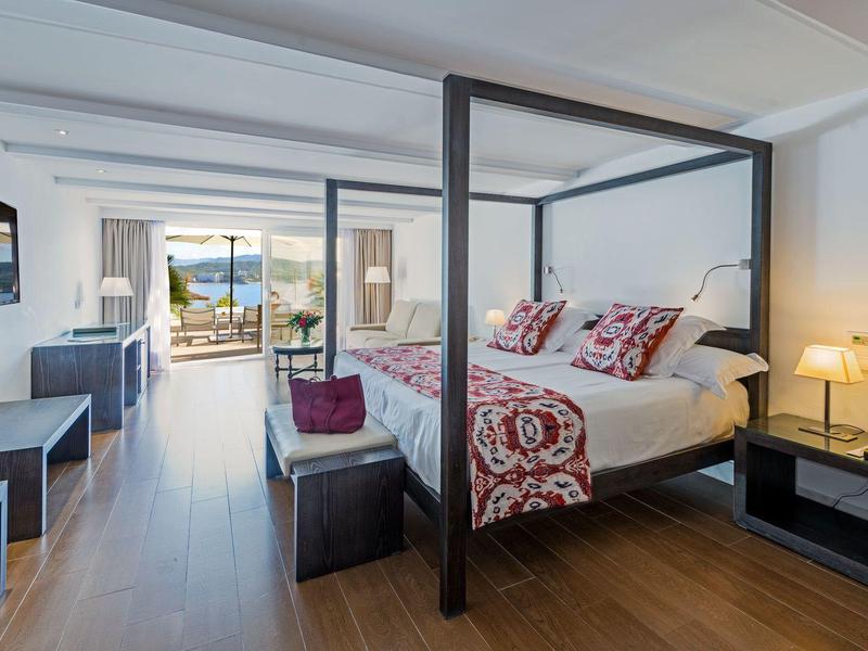 Chambre d'hôtel moderne avec lit à baldaquin, télévision écran plat et balcon vue mer.