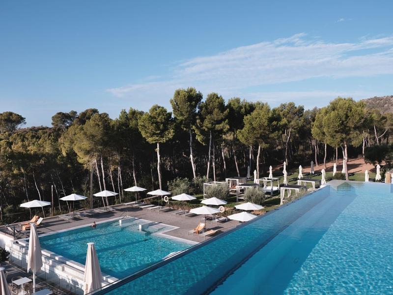 Deux piscines avec parasols et arbres en arrière-plan sous un ciel bleu.