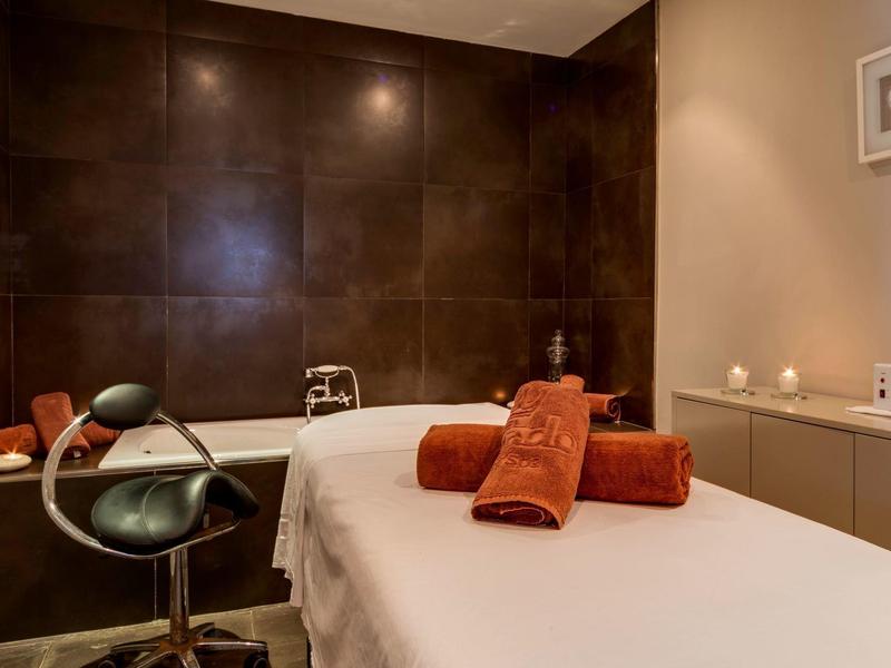 Espace bien-être confortable avec table de massage, deux serviettes orange et lumière douce.