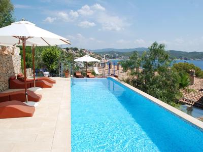Piscina infinita con tumbonas y sombrillas con vistas al mar y colinas verdes.