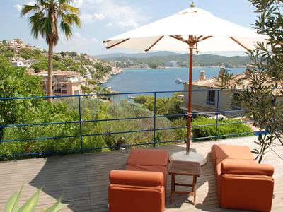 Terraza con muebles rojos, sombrilla y vista a un paisaje costero con agua y colinas.