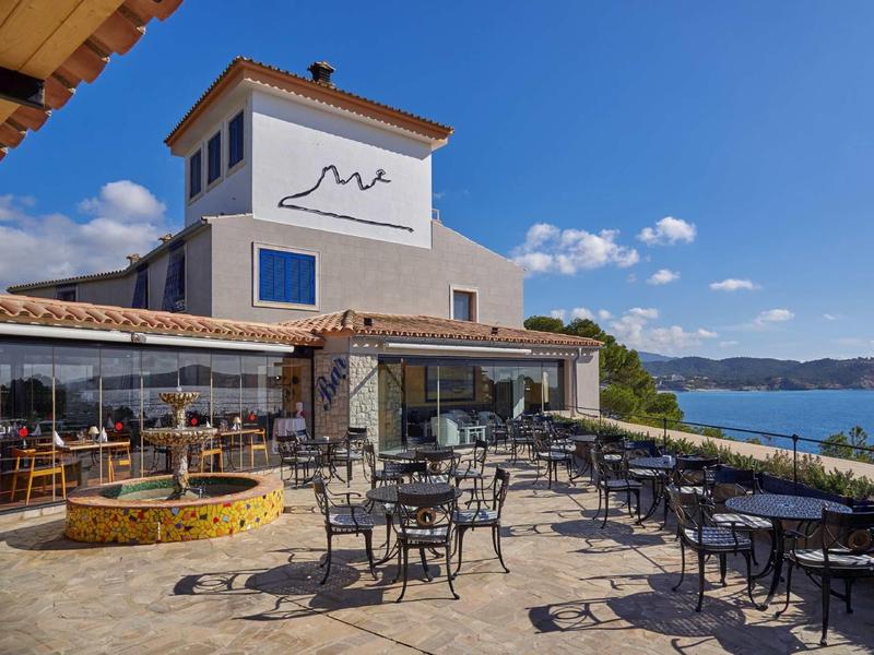 Terraza de restaurante junto al mar con mesas y sillas de metal en un día soleado