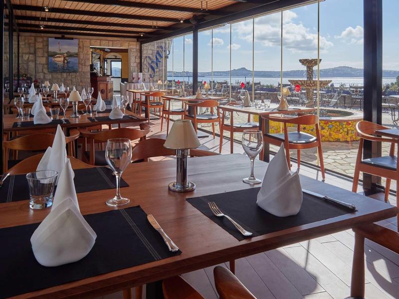 Restaurante elegante con mesas de madera y vista al agua y montañas a través de grandes ventanas.