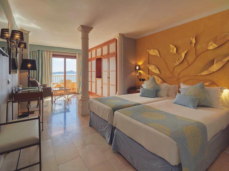 Habitación de hotel con dos camas individuales, pared decorativa, escritorio y vista a balcón con vista al mar.