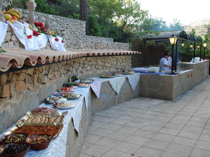 Buffet con diferentes comidas al aire libre frente a un muro de piedra y árboles.