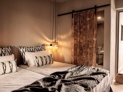 Gemütliches Schlafzimmer mit Doppelbett, gemusterten Kissen, hängender Lampe und braunem Vorhang.