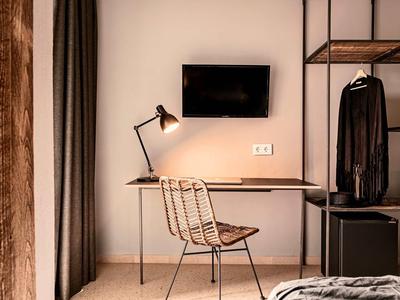 Moderner Arbeitsplatz mit Metallstuhl, Holzschreibtisch, Lampe, Wand-TV und offener Kleiderstange.