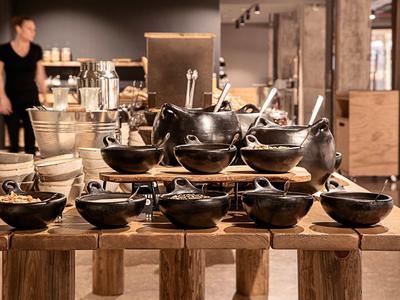 Schwarze Keramikschalen und Töpfe in verschiedenen Größen auf Holztisch, Verkaufsraum im Hintergrund.