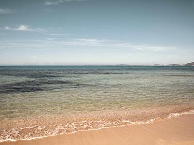 Klarer Himmel über ruhigem, flachem Meer mit sanften Wellen und hellem Sandstrand im Vordergrund.