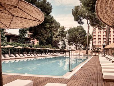 Schwimmbad mit klar blauem Wasser, weißen Liegestühlen und großen Sonnenschirmen aus Stroh.