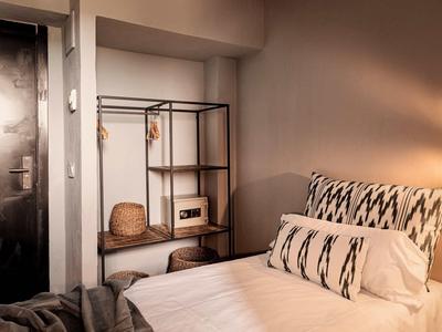 Gemütliches Zimmer mit Einzelbett, gemusterten Kissen, schwarzem Regal und geschlossenem Eingangstür.