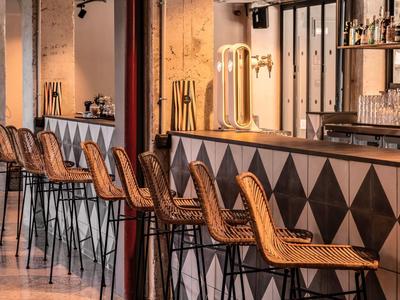 Moderner Barbereich mit hohen Stühlen, geometrischen Fliesen und warmem Licht an der Theke.