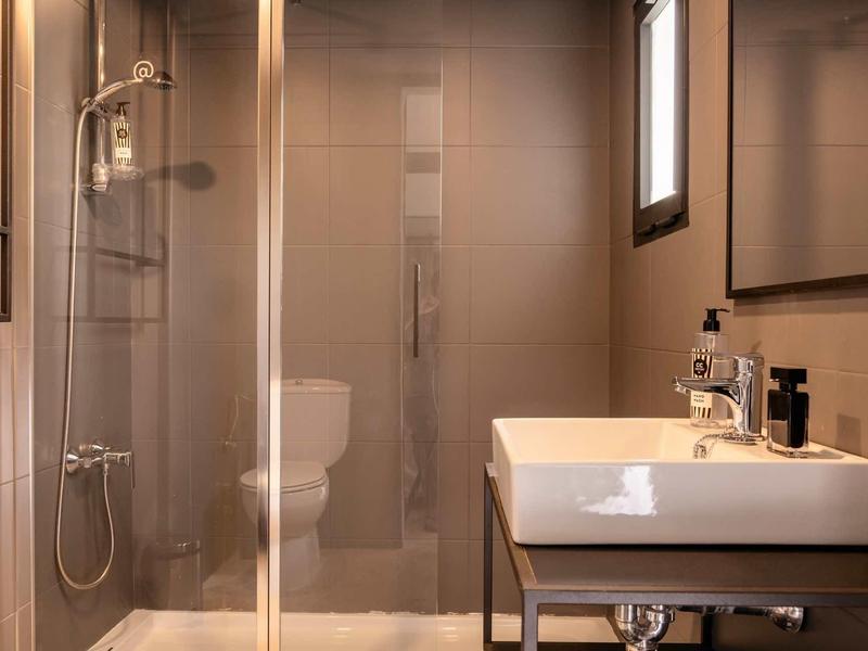 Modernes Badezimmer mit Glasdusche, weißem Waschbecken, Spiegel und beigem Fliesendesign.