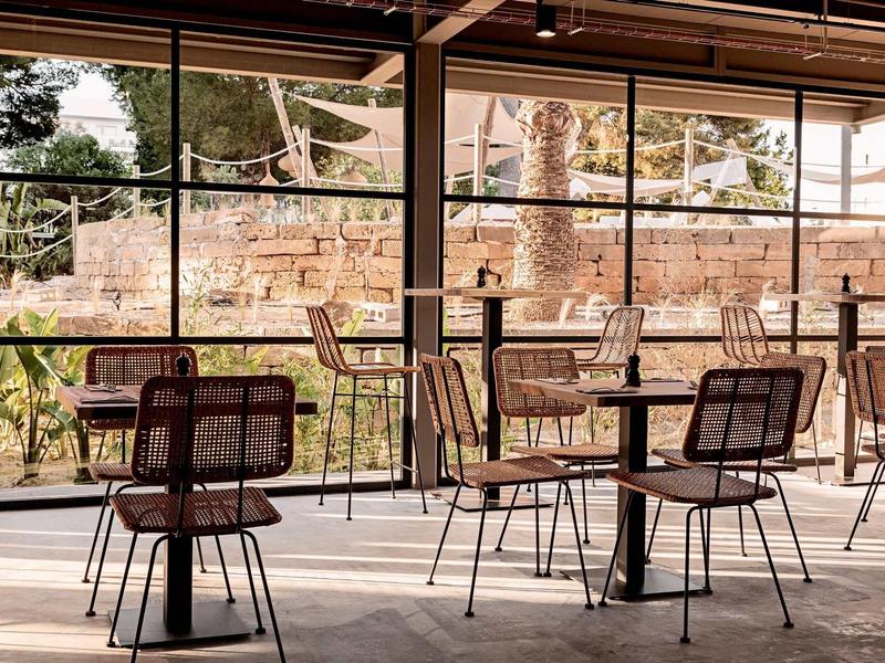 Leerer Innenbereich eines Cafés mit Metallstühlen und Holztischen vor großen Fenstern.