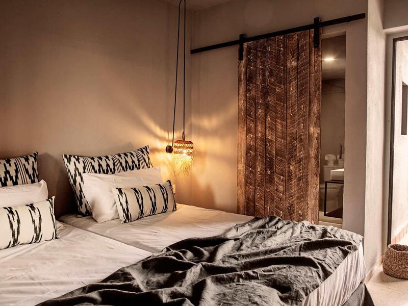 Gemütliches Schlafzimmer mit Doppelbett, gemusterten Kissen, hängender Lampe und braunem Vorhang.