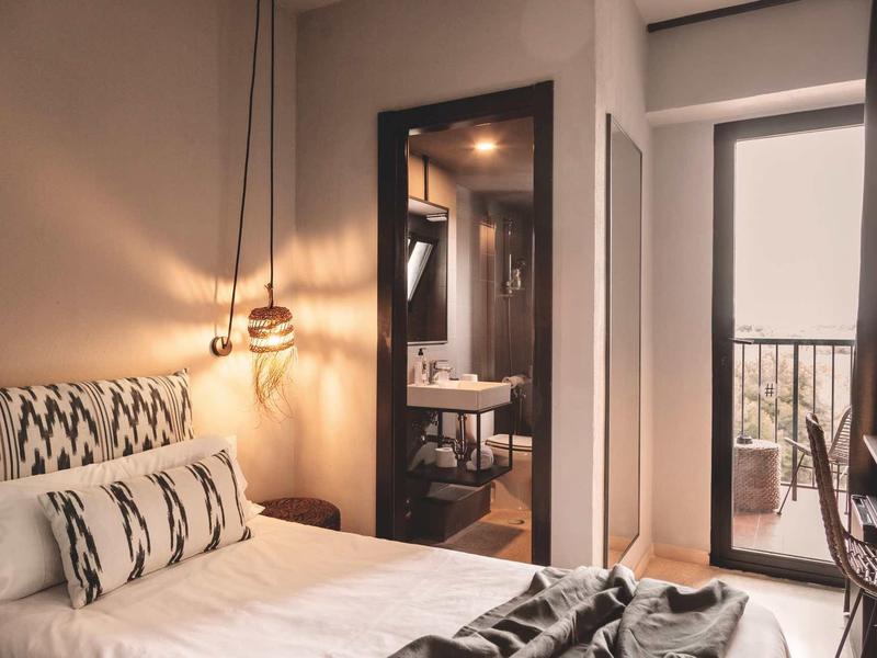 Gemütliches Schlafzimmer mit hellen Wänden, großem Bett, Hängelampe und Blick auf Balkon.