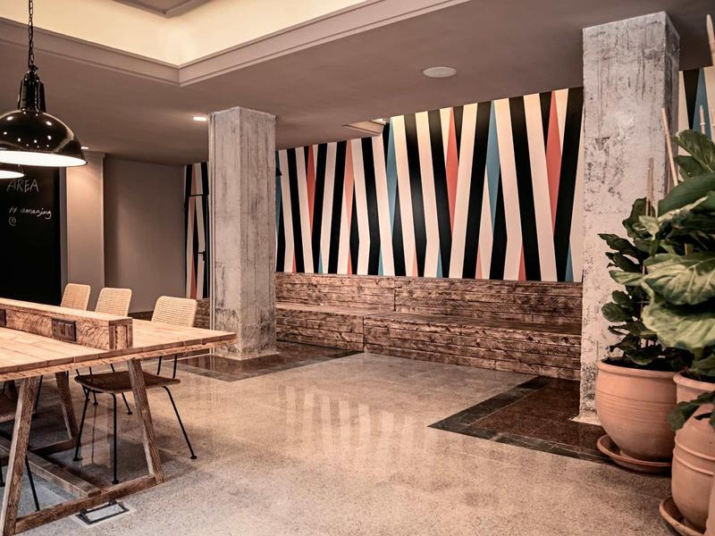 Moderner Innenraum mit Holztisch, Metallstühlen, Betonboden und gestreifter Wanddekoration.