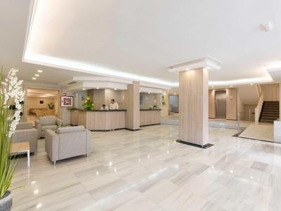 Luminoso e moderno atrio d'hotel con area salotto, reception e piante.