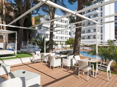 Terrazza dell'hotel con sedie bianche, tavoli e piscina in un ambiente urbano soleggiato.
