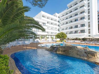 Hotel con edificio bianco, piscina con rocce e palme in primo piano