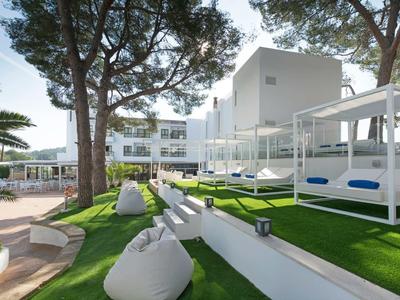 Area esterna moderna di un hotel con lettini, pouf e grandi alberi su prato curato.