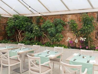 Moderne buitenruimte van een hotel met witte tafels, stoelen en een groene stenen muur.