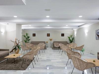 Moderne lounge met stoelen, tafels en planten op lichte marmeren vloer in een hotel.