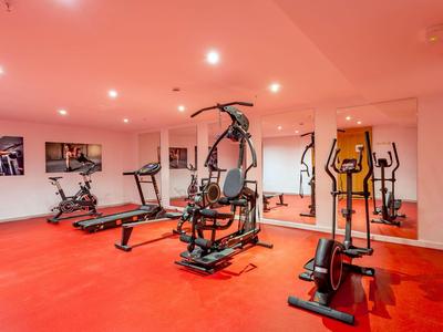 Fitnessruimte met verschillende fitnessapparaten en rode vloer.