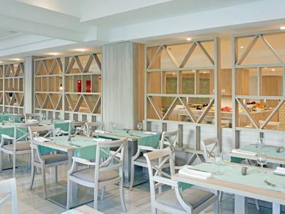 Lichte restaurant met moderne witte tafels en grijze stoelen, decoratieve houten afscheidingen.