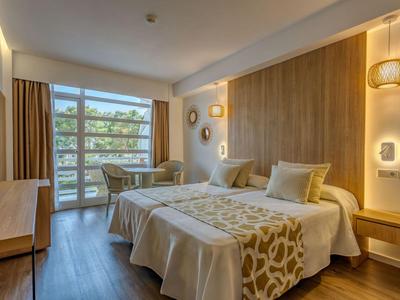 Lichte hotelkamer met tweepersoonsbed, houten wandbekleding en balkon met uitzicht op bomen.
