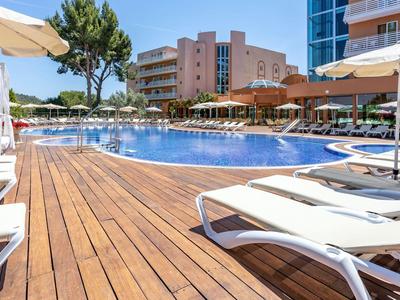 Hotelzwembad met houten dek en witte ligbedden onder parasols op een zonnige dag.