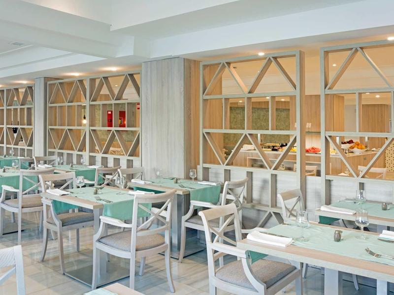 Sala da pranzo moderna con tavoli e sedie bianchi in un ambiente alberghiero luminoso.