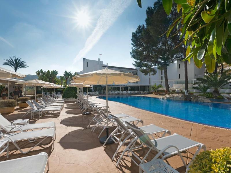 Area piscina soleggiata con lettini e ombrelloni accanto a un edificio alberghiero.