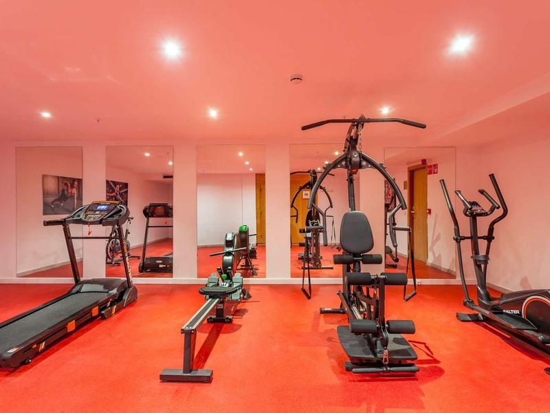 Una palestra moderna con pavimenti rossi, tapis roulant, vogatore e varie attrezzature per allenamento.