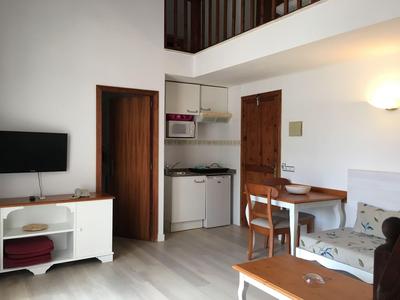 Kleines Hotelzimmer mit Fernseher, Tisch, Stühlen und Küchenzeile mit Mikrowelle.