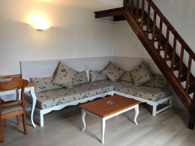 Gemütliche Sitzecke mit gepolstertem Ecksofa und Holztisch unter einer Treppe in einem Hotelzimmer.