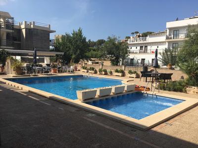 Dos piscinas en un complejo hotelero con edificios y plantas alrededor.