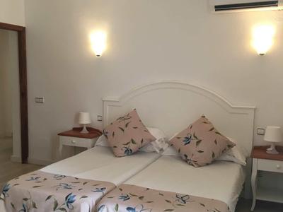 Camera doppia con copriletto floreale, due cuscini, comodini e applique da parete.