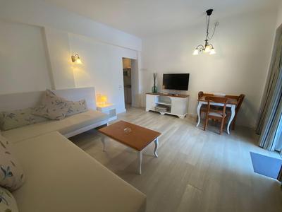 Helles Hotelzimmer mit Sofa, Couchtisch, Fernseher und kleinem Schreibtisch mit Stuhl.