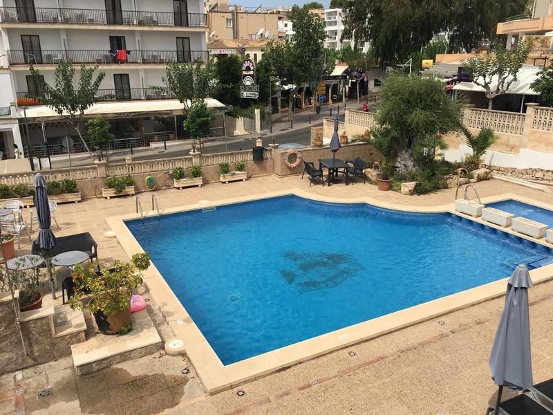 Čtvercový venkovní bazén s modrou vodou, obklopený lehátky a slunečníky.