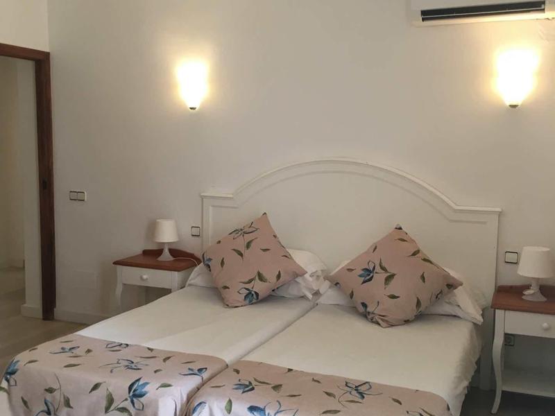 Dvoulůžkový pokoj s květinovým přehozem, dvěma polštáři, nočními stolky a nástěnnými lampami.